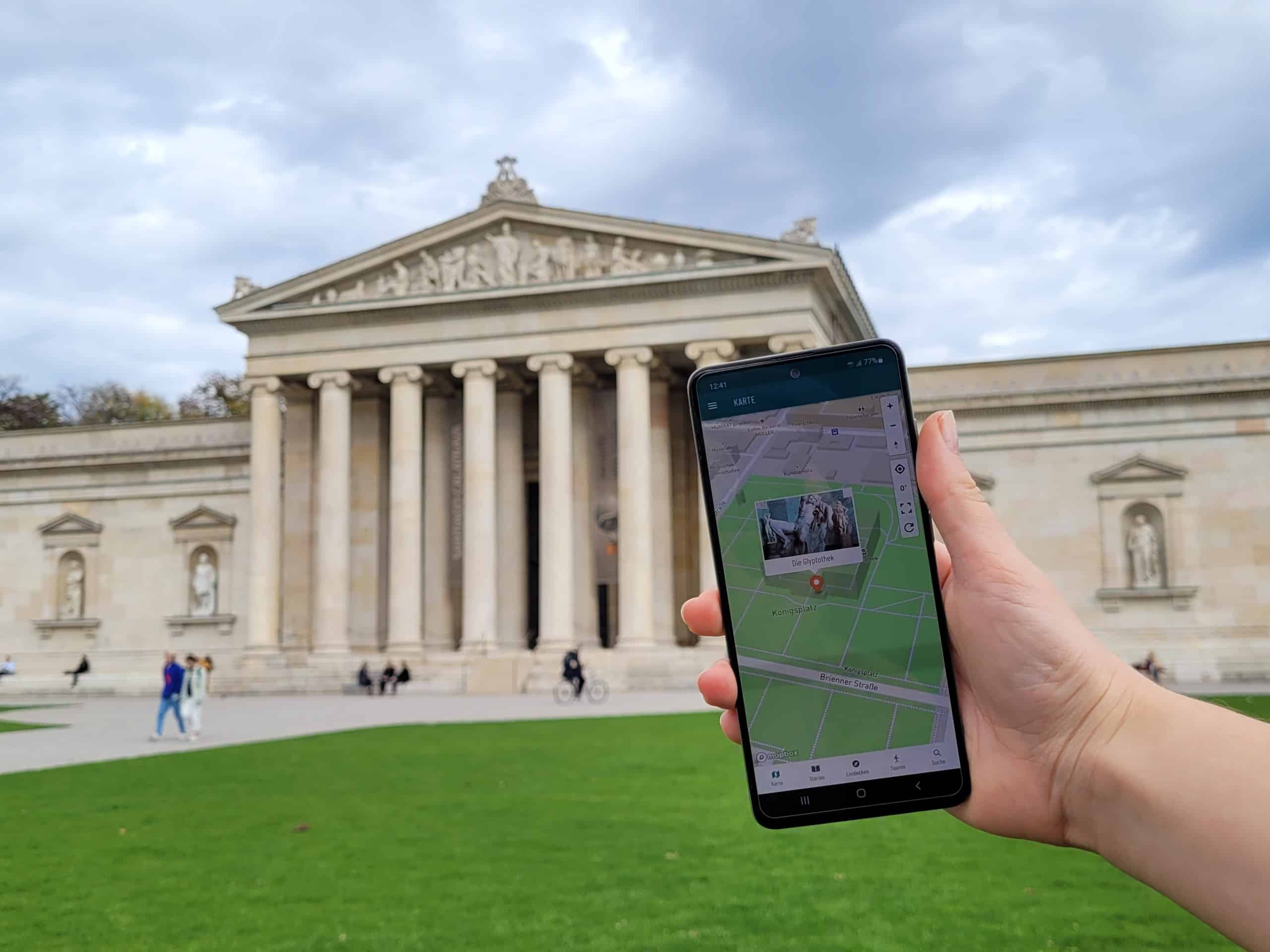 Eine Frau hält ein Smartphone mit der geöffneten App vor der Münchner Glyptothek in die Höhe. Foto: Alexandra Avrotina